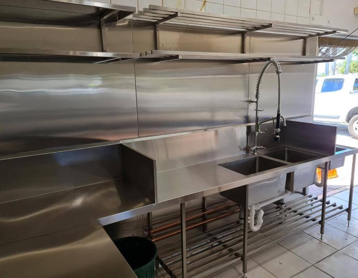 A stainless sink run and overhead shelving in a commercial kitchen