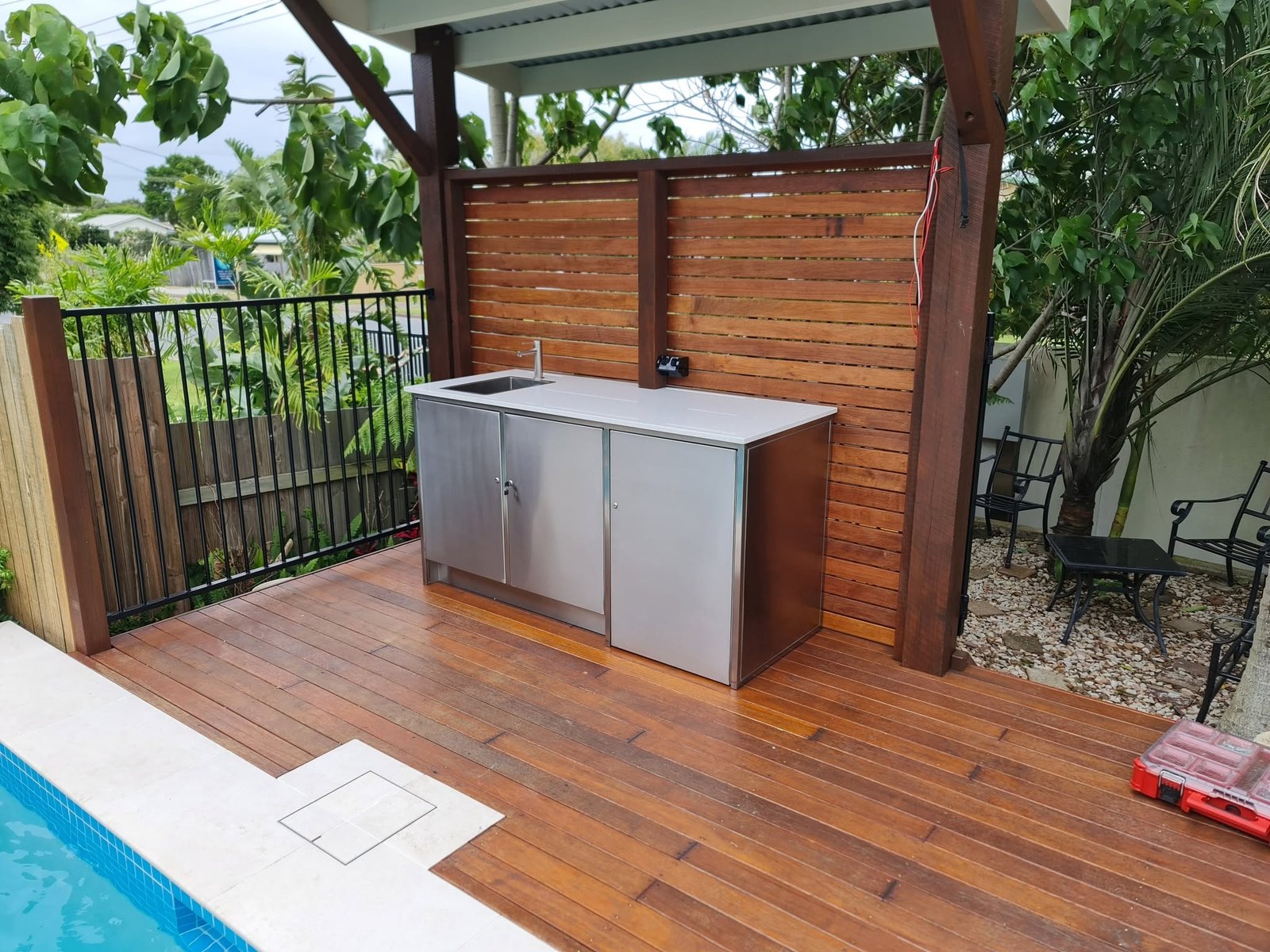 A stainless outdoor kitchen unit on a poolside deck