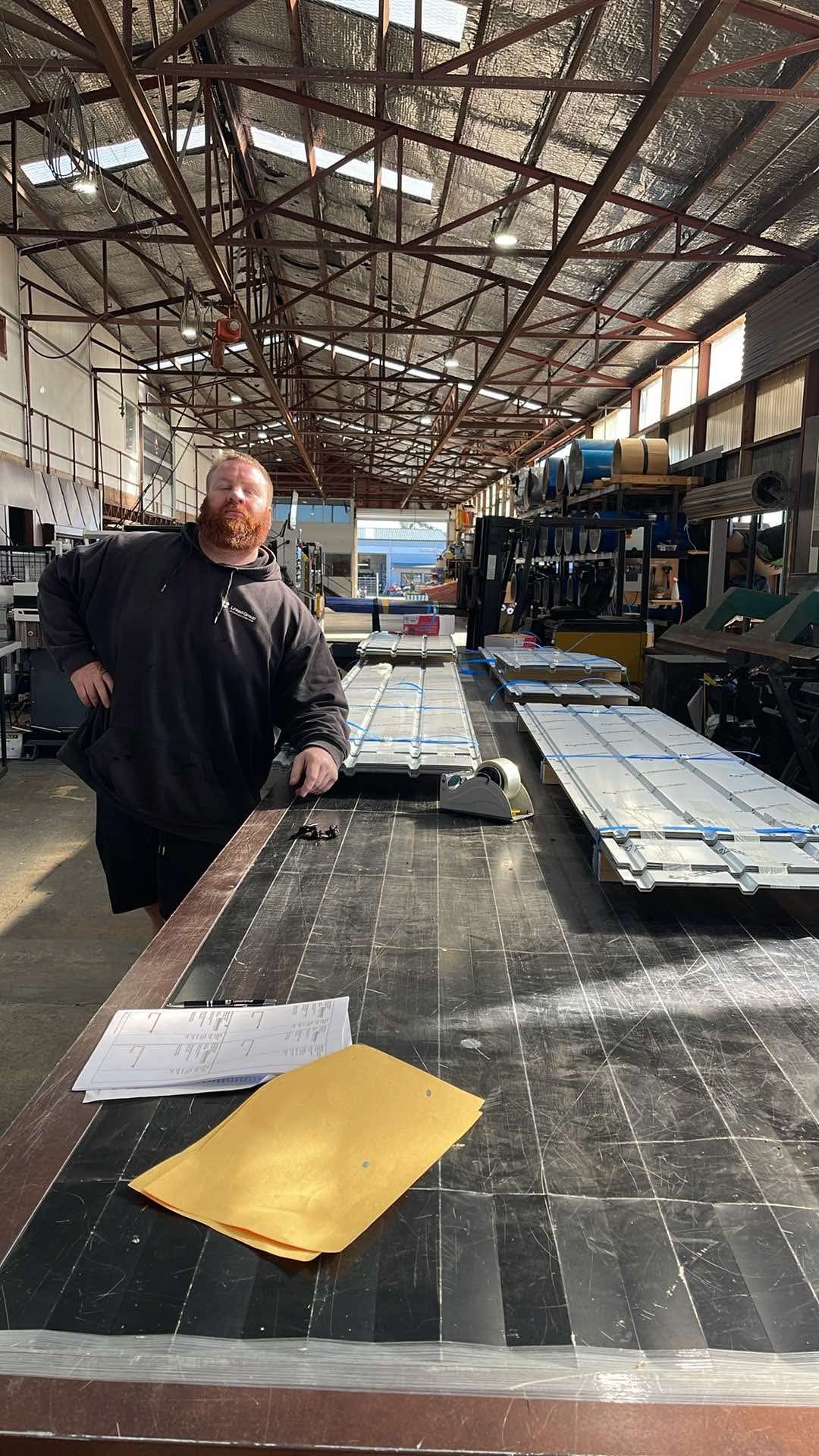 A Linked Group team member checking job paperwork against stacked roofing panels in the Matamata workshop