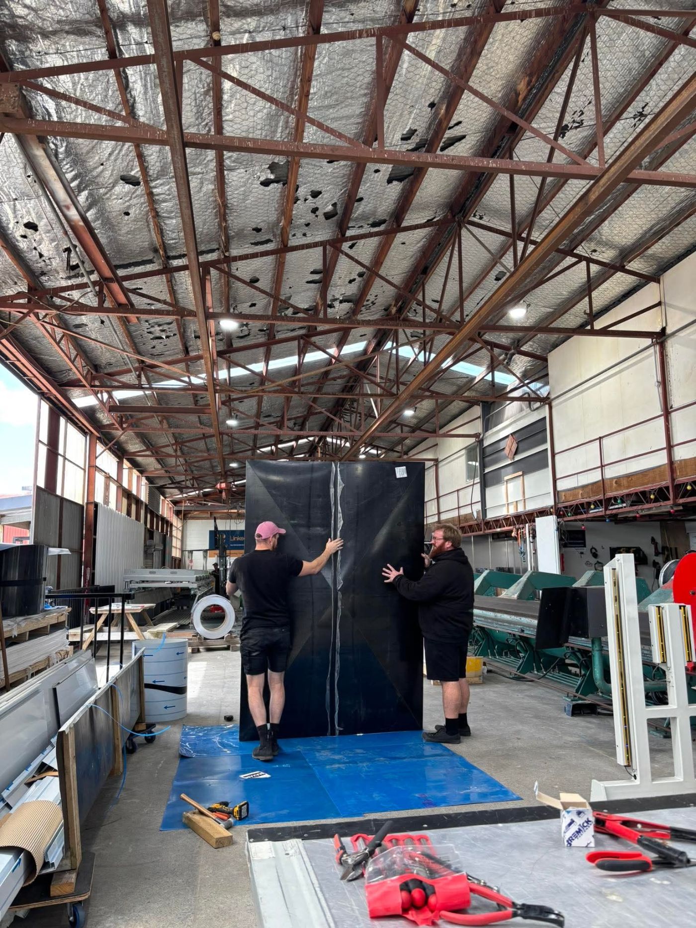 Two Linked Group team members handling a large cladding panel in the workshop
