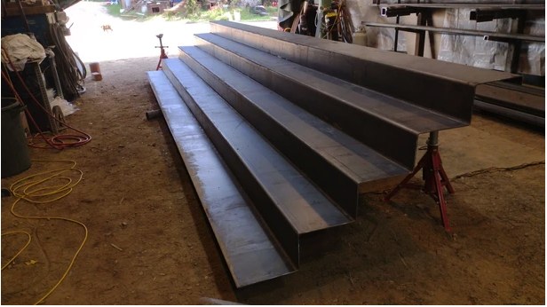 Bent steel channel stock staged on stands in the Mayne Island Metal shop