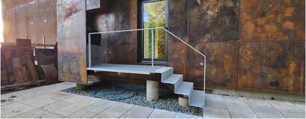 A finished steel-and-glass entry landing against a corten wall