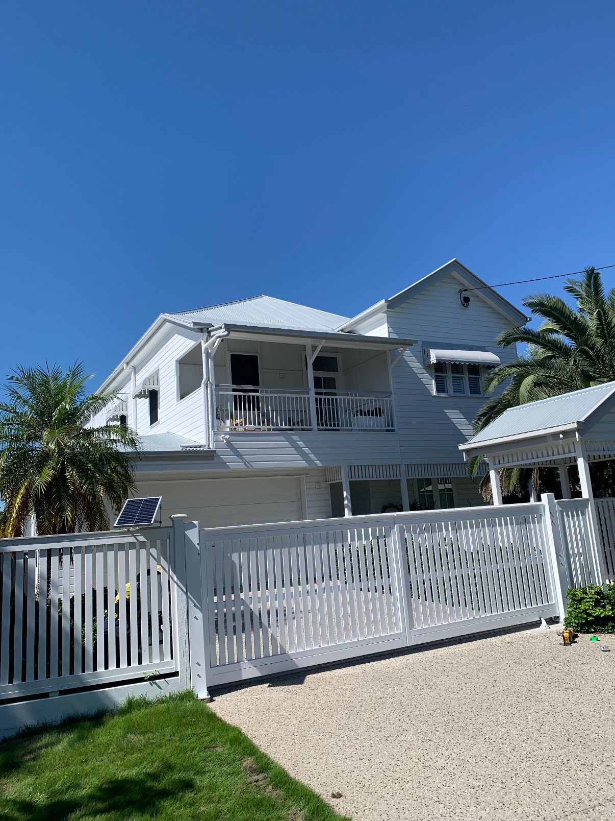 White aluminium slat driveway gates and matching fence on a weatherboard home