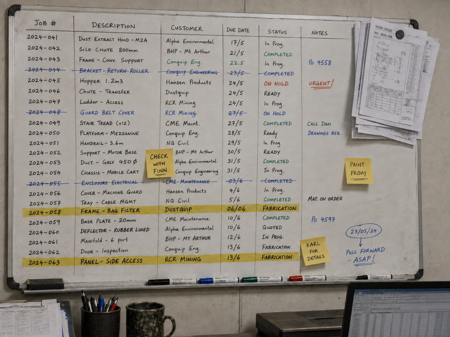 Job tracking whiteboard in a fab shop office, job numbers and due dates written up by hand with sticky notes and highlighter
